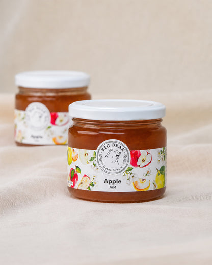 Two glass jars of Big Bear Farms Apple Jam on a beige fabric background, with the front jar in sharp focus and the rear jar softly blurred.