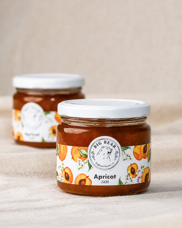 Two glass jars of Big Bear Farms Apricot Jam on a beige fabric background, with one jar in sharp focus in the foreground and the other blurred in the background.