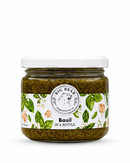 A jar of Big Bear Farms Basil in a Bottle pesto, featuring a white lid and a white label decorated with green basil leaves and orange garlic cloves, set against a plain white background.