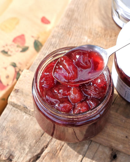 Big Bear Farms cherry preserve being scooped out with a spoon showing the glossy texture of whole cherries preserved in a glass jar