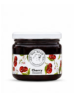 A glass jar of Big Bear Farms Cherry Preserve with a white lid and a white label decorated with red cherries and green leaves, set against a plain white background.