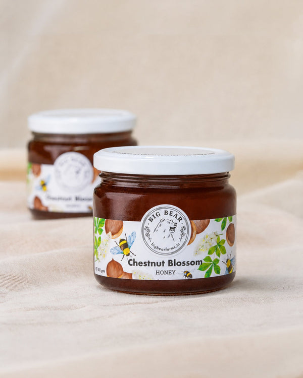 Two glass jars of Big Bear Farms Chestnut Blossom Honey arranged on a beige fabric surface, with one jar in sharp focus in the foreground and the other softly blurred in the background.