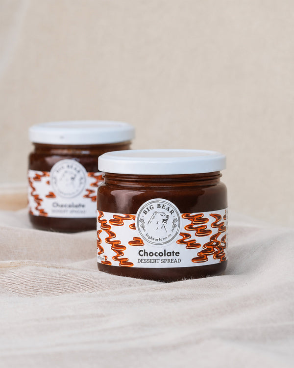 Two glass jars of Big Bear Farms Chocolate Dessert Spread on a beige fabric surface, with one jar in sharp focus in the foreground and the other softly blurred in the background.