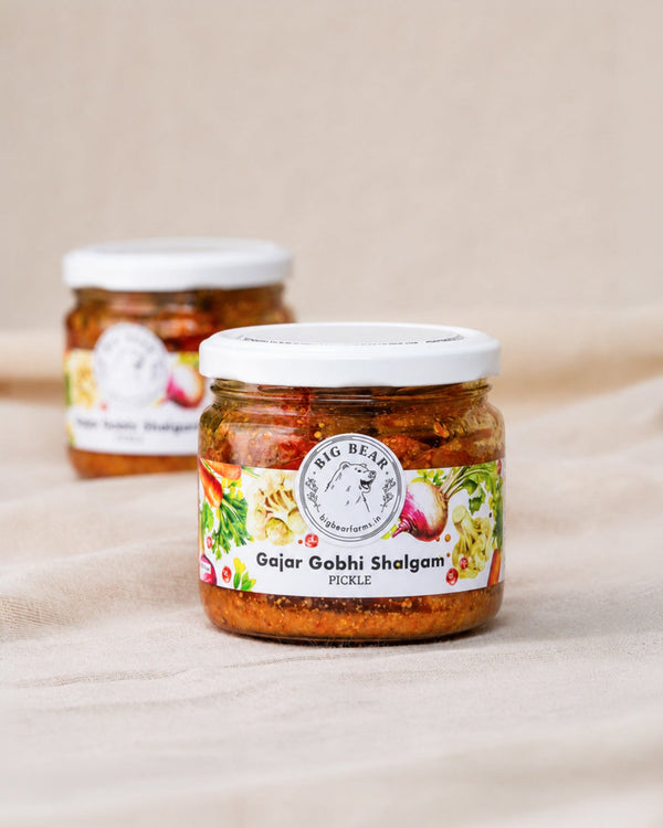 Two glass jars of Big Bear Pickles Gajar Gobhi Shalgam Pickle arranged on a beige fabric surface, with the front jar in sharp focus and the rear jar softly blurred. Carrot Radish Cauliflower pickle.