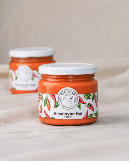 Two glass jars of Big Bear Farms Fiery Himalayan Hot Sauce on a neutral beige fabric background, with the front jar in sharp focus and the rear jar softly blurred.