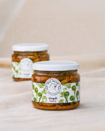 Two glass jars of Big Bear Farms Lingdi Pickle (fiddlehead fern pickle) on a neutral beige fabric background, with one jar in sharp focus in the foreground and the other softly blurred in the background.