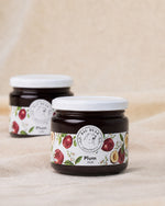 Two glass jars of Big Bear Farms Plum Jam on a beige fabric background, with one jar in sharp focus in the foreground and the other softly blurred in the background.
