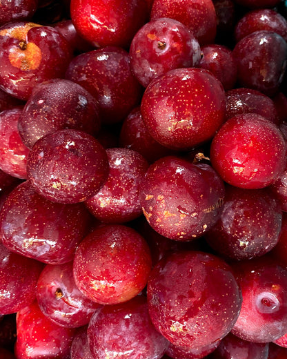 A close-up pile of glossy red cherries with visible skin and small speckles, filling the frame. Big Bear Farms Plum Chutney