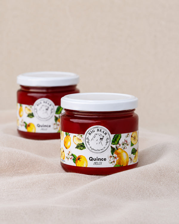 Two glass jars of Big Bear Farms Quince Jelly with white lids, displayed on a beige fabric surface with a matching background.