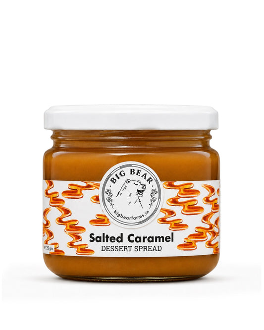A jar of Big Bear Farms Salted Caramel Dessert Spread on a clean white background. The product is in a clear glass jar showing the golden-brown caramel spread inside, topped with a white lid and featuring a white label with orange caramel swirl illustrations.