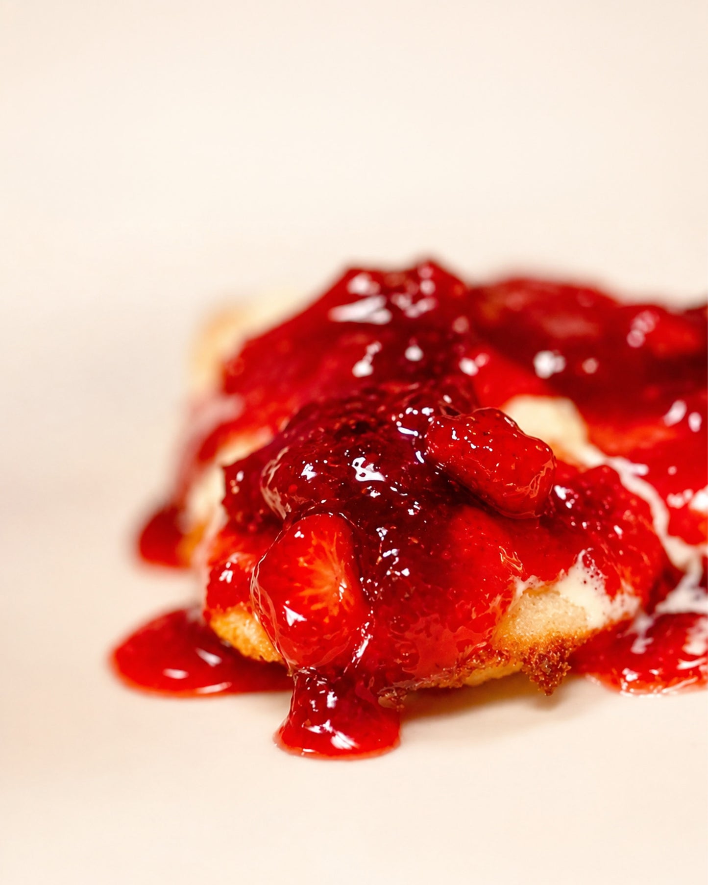 A close-up shot of a strawberry dessert, featuring a golden-brown biscuit topped with a glossy, rich red strawberry jam, set against a clean, light beige background using Big Bear Farms Strawberry Jam