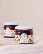 Two glass jars of Big Bear Farms Strawberry Jam arranged on a draped beige fabric surface against a neutral beige background.