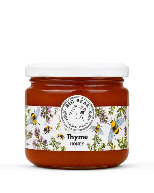 A jar of Big Bear Farms Thyme Honey on a clean white background. The jar contains amber-colored honey and features a white lid and a decorative label with illustrations of bees, flowers, and herbs.