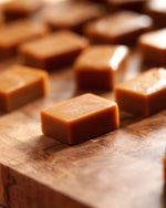 Several glossy brown Big Bear Farms buttery caramel toffees arranged on a wooden surface, with a shallow depth of field focusing on the foreground piece.
