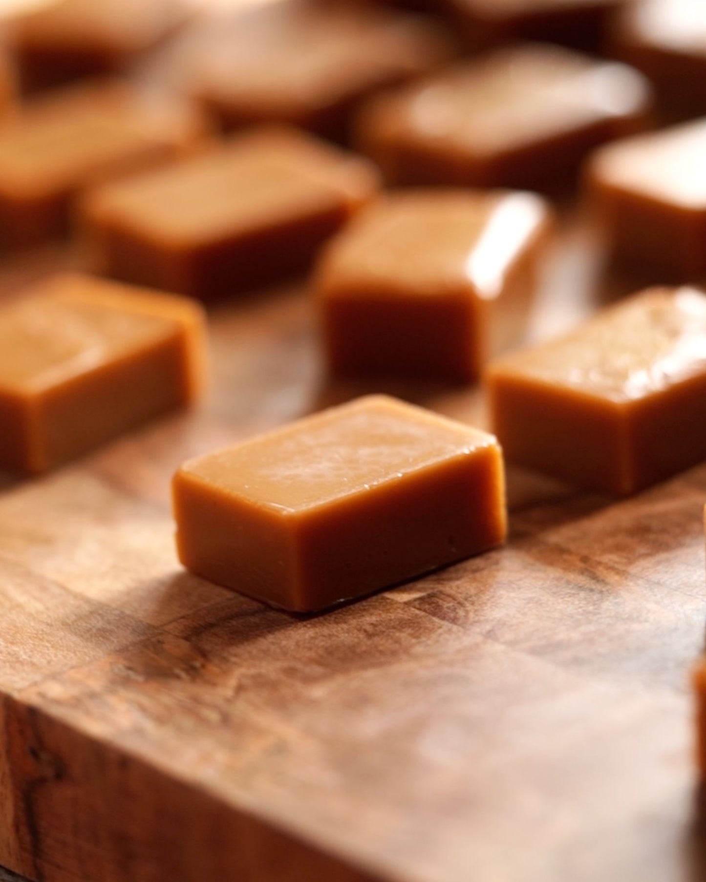 Several glossy brown Big Bear Farms buttery caramel toffees arranged on a wooden surface, with a shallow depth of field focusing on the foreground piece.